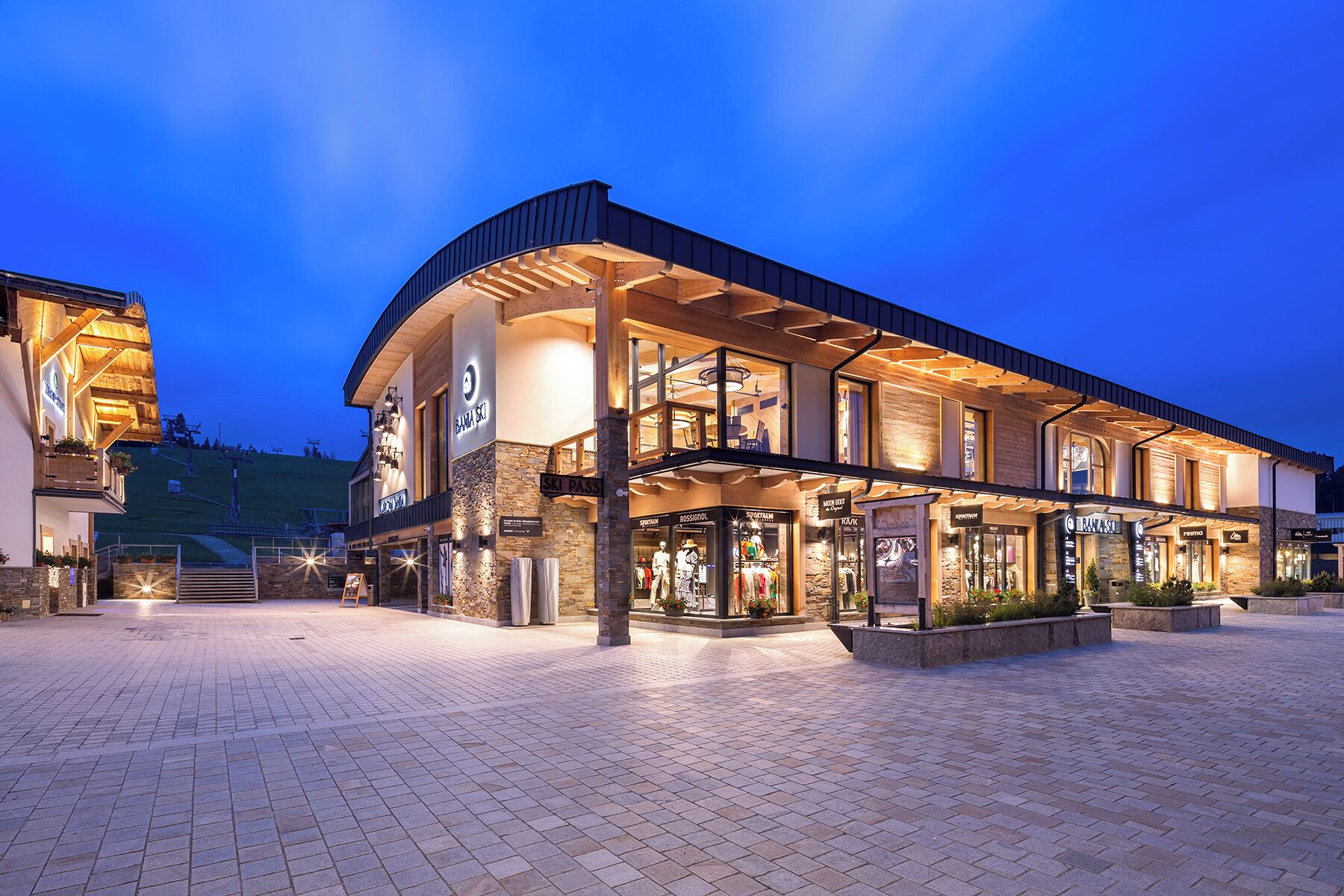 Un hotel moderno con fachada de piedra, varios pisos y un área exterior cubierta con tiendas.