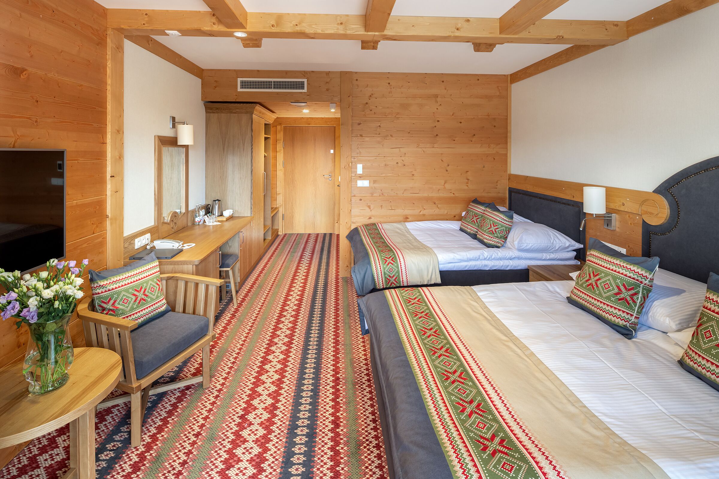 A wooden room with two beds, a desk, and a TV.