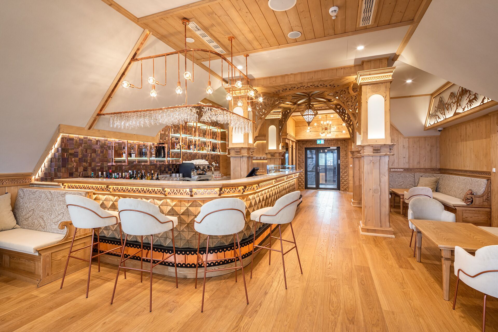 A bar area with a wooden ceiling, a bar counter with shelves of bottles, and a seating area with chairs and a table.