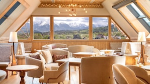 A cozy room with a wooden ceiling, large windows, and a view of snow-capped mountains. - Hotel Bania Thermal & Ski (Bukowina Tatrzanska)