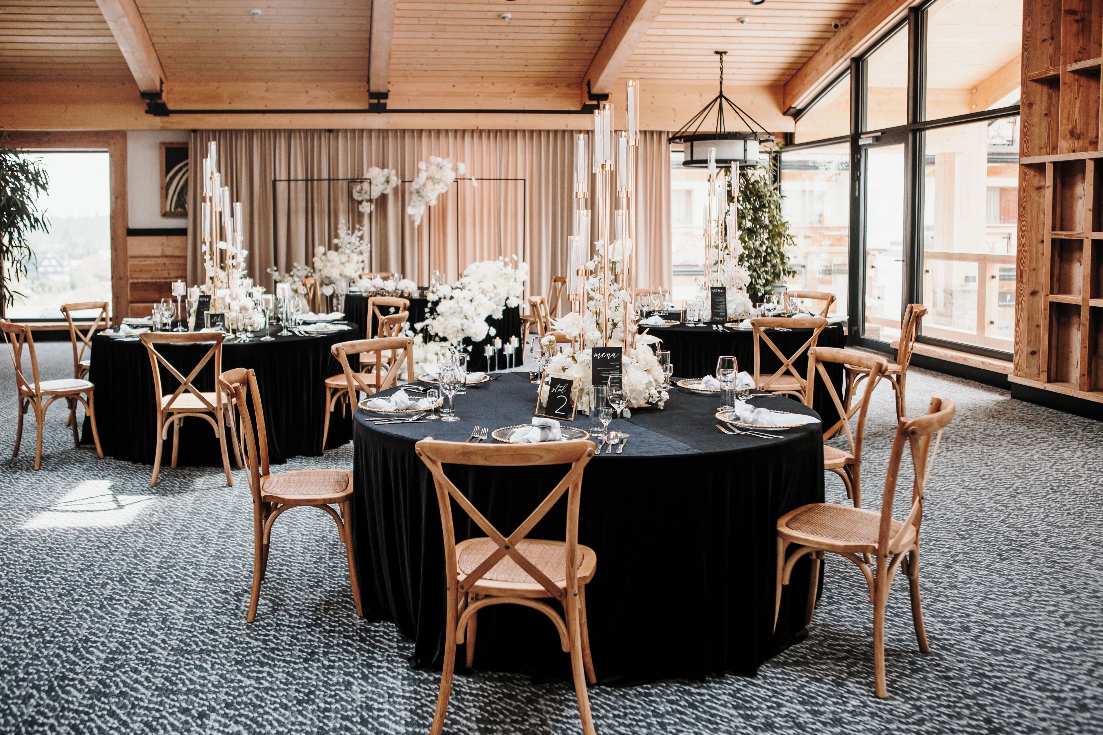 A round table with black tablecloths, wooden chairs, and white floral arrangements.