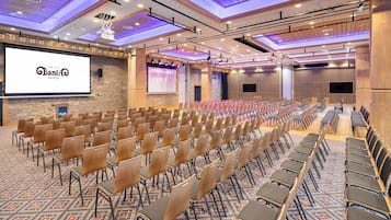 Un salón de conferencias con filas de sillas, una pantalla grande y un proyector.
