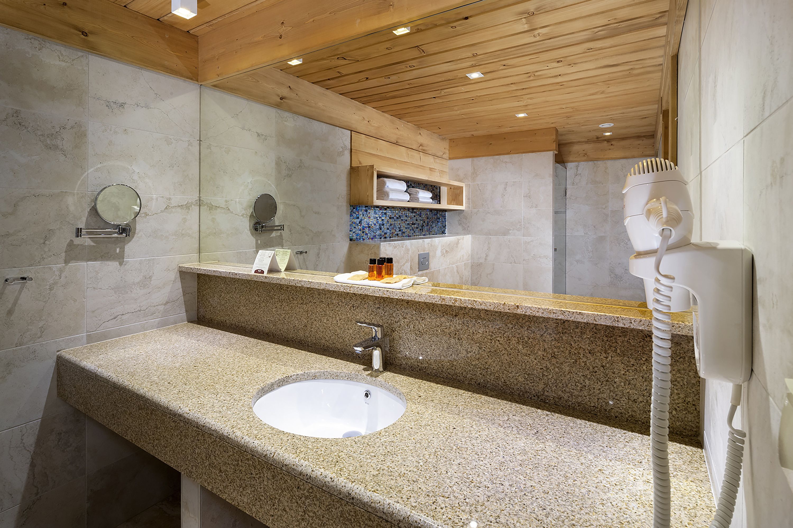 A bathroom with a granite countertop sink, a mirror, a towel rack, and a hairdryer.