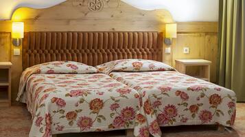 A double bed with floral bedding, a wooden headboard, two bedside tables with lamps, and a wooden nightstand.