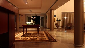 A spacious lobby with a patterned carpet, a wooden table with flowers, and a seating area with chairs. - Palazzo Giordano Bruno (Nola)