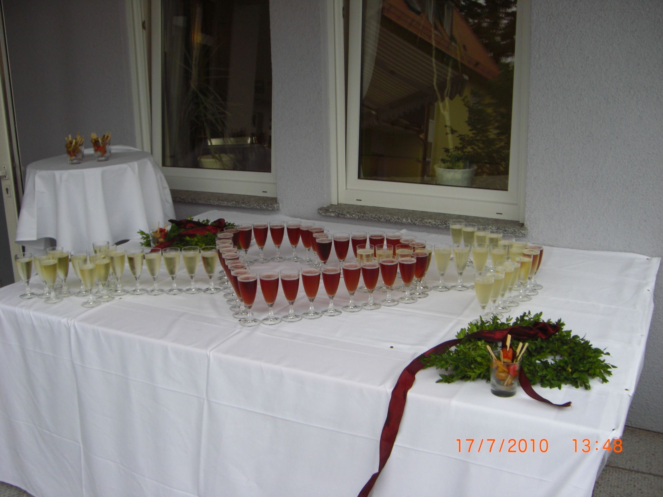 Una mesa servida con varios vasos de bebidas, una pequeña mesa con mantel blanco y una ventana al fondo.
