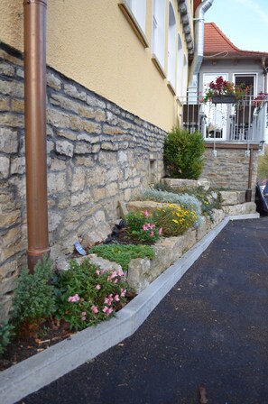 Eine Steinsäule mit Blumenbeet und einem Metallfallrohr an der Gebäudeseite.