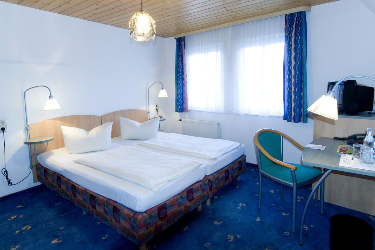 A hotel room with a double bed, a desk with a chair, a television, and a window with curtains.