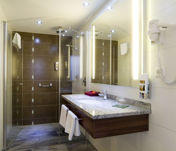 Un baño moderno con ducha acristalada, lavamanos de mármol y un espejo grande.