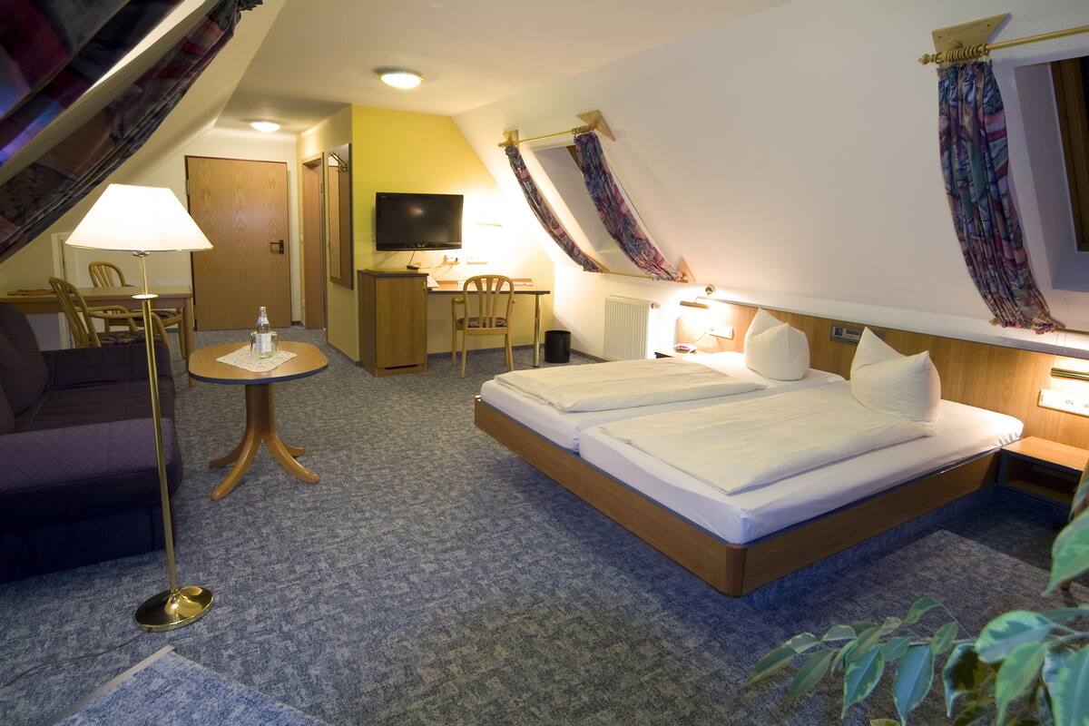 A hotel room with a bed, a desk, a chair, a TV, and a lamp.