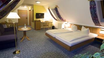 A hotel room with a bed, a desk, a chair, a TV, and a lamp.