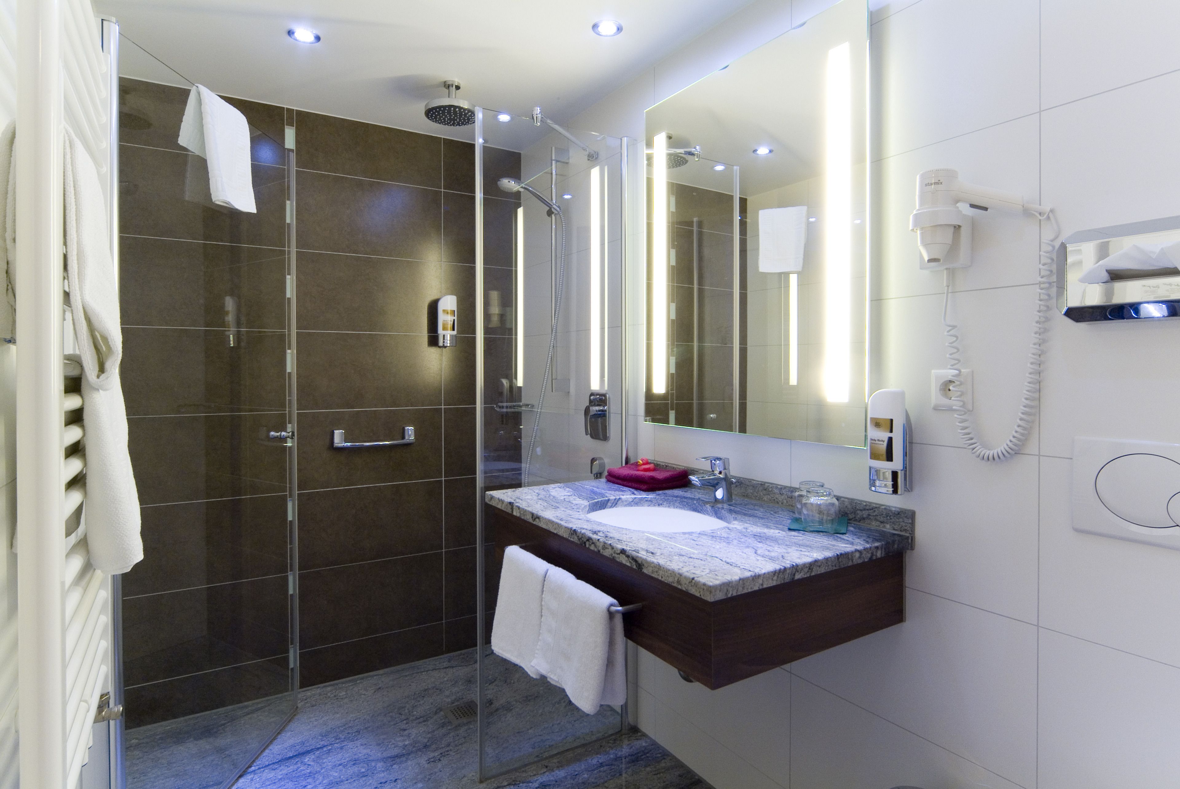 A modern bathroom with a glass-enclosed shower, a marble sink, and a large mirror.