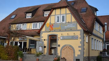 A hotel with a yellow facade, a signboard, and a traditional roof.