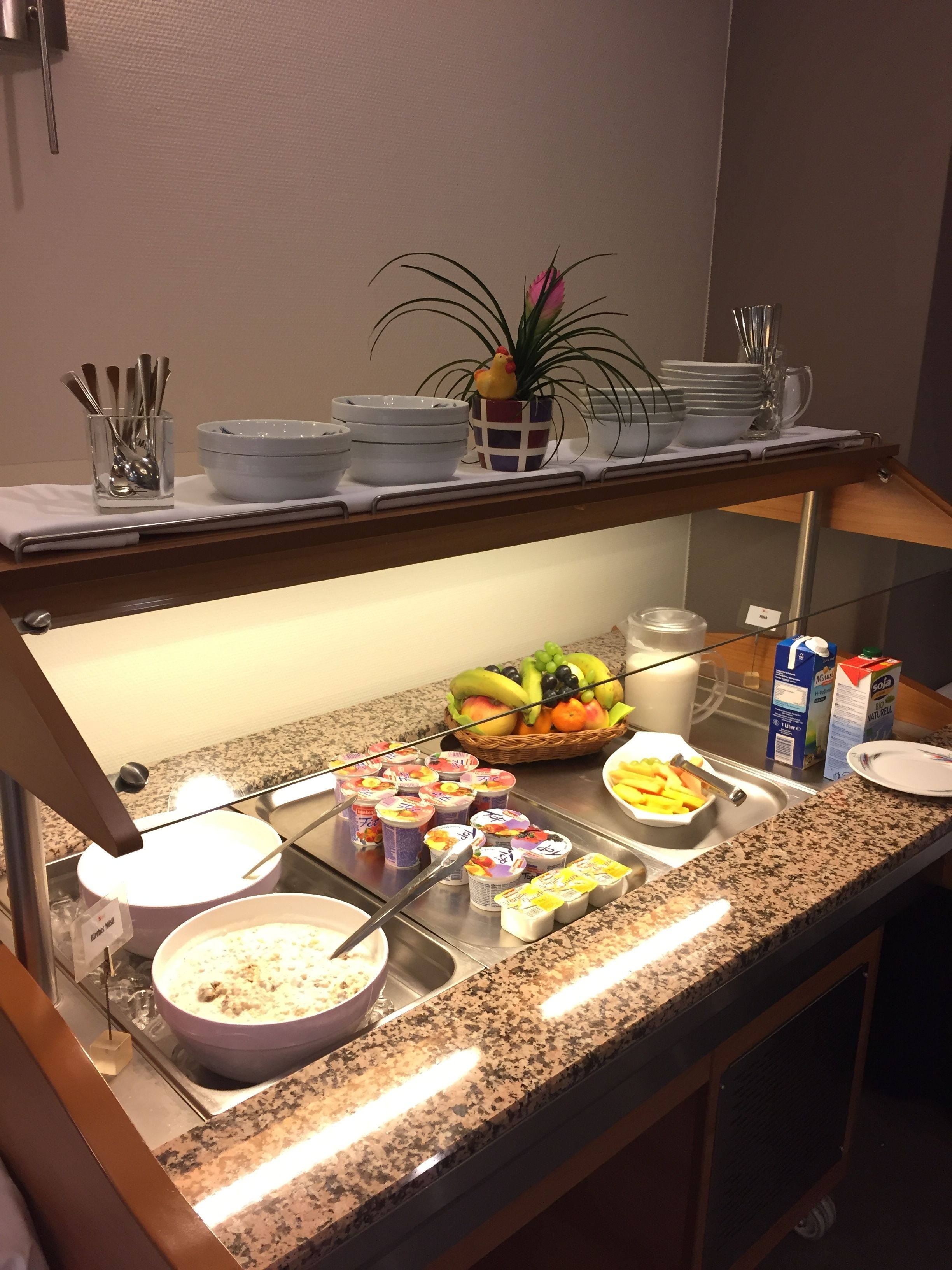 A buffet setup with various food items, including fruits, yogurt, and a bowl of soup.