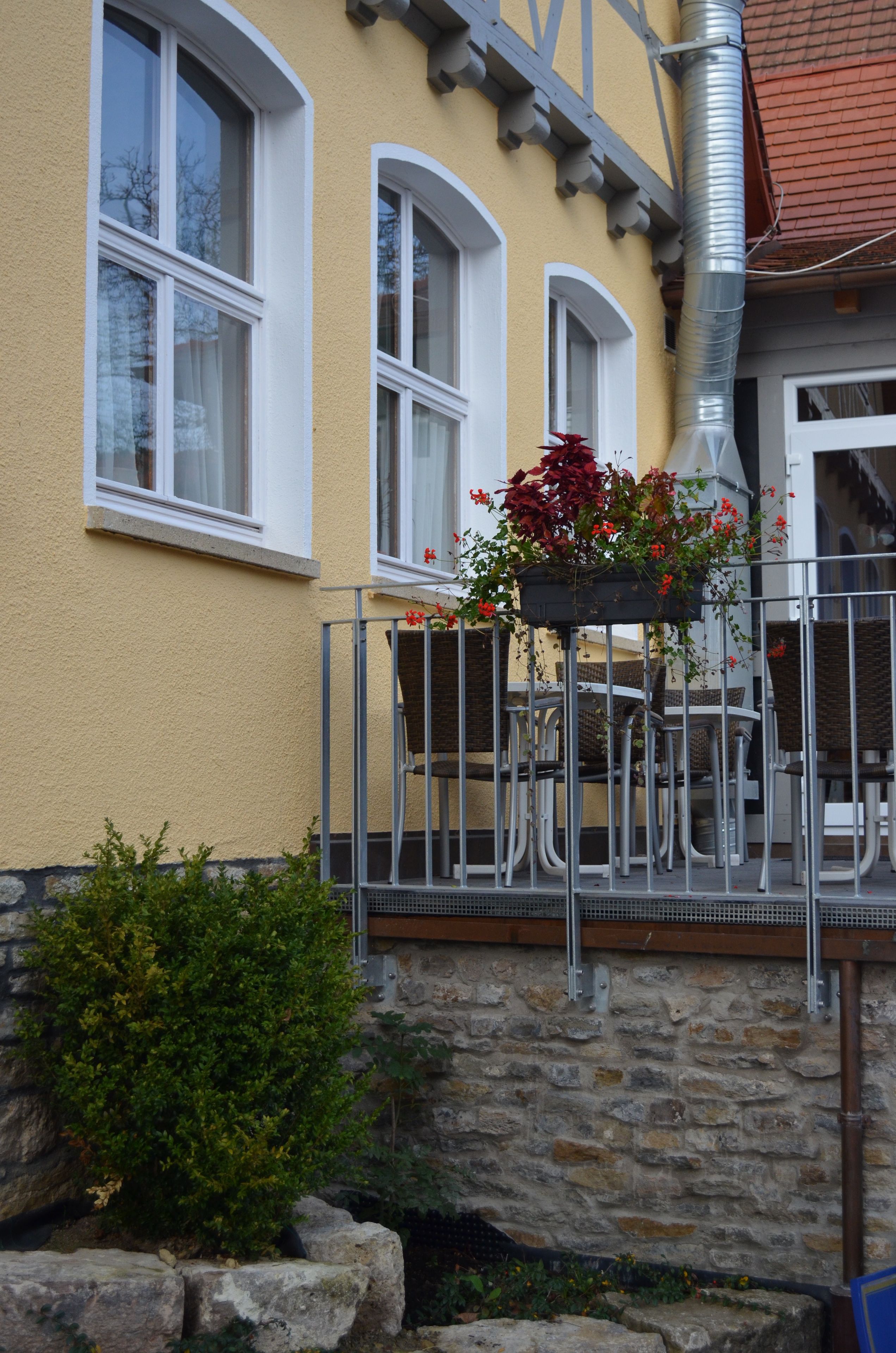 A building with a yellow facade, white-framed windows, a stone base, and a metal railing.