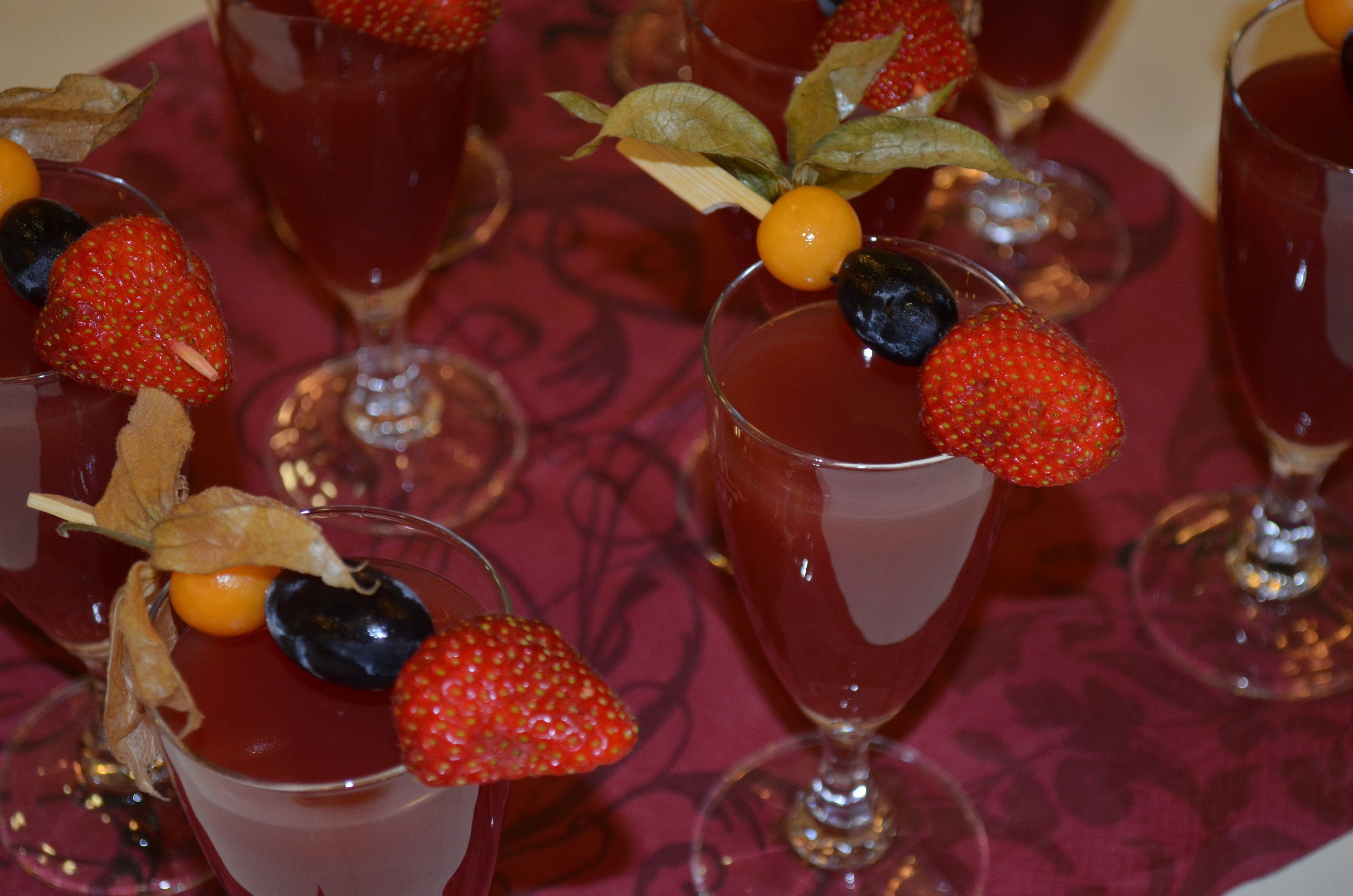 A table with multiple glasses of red beverage, each garnished with a strawberry and a blueberry.