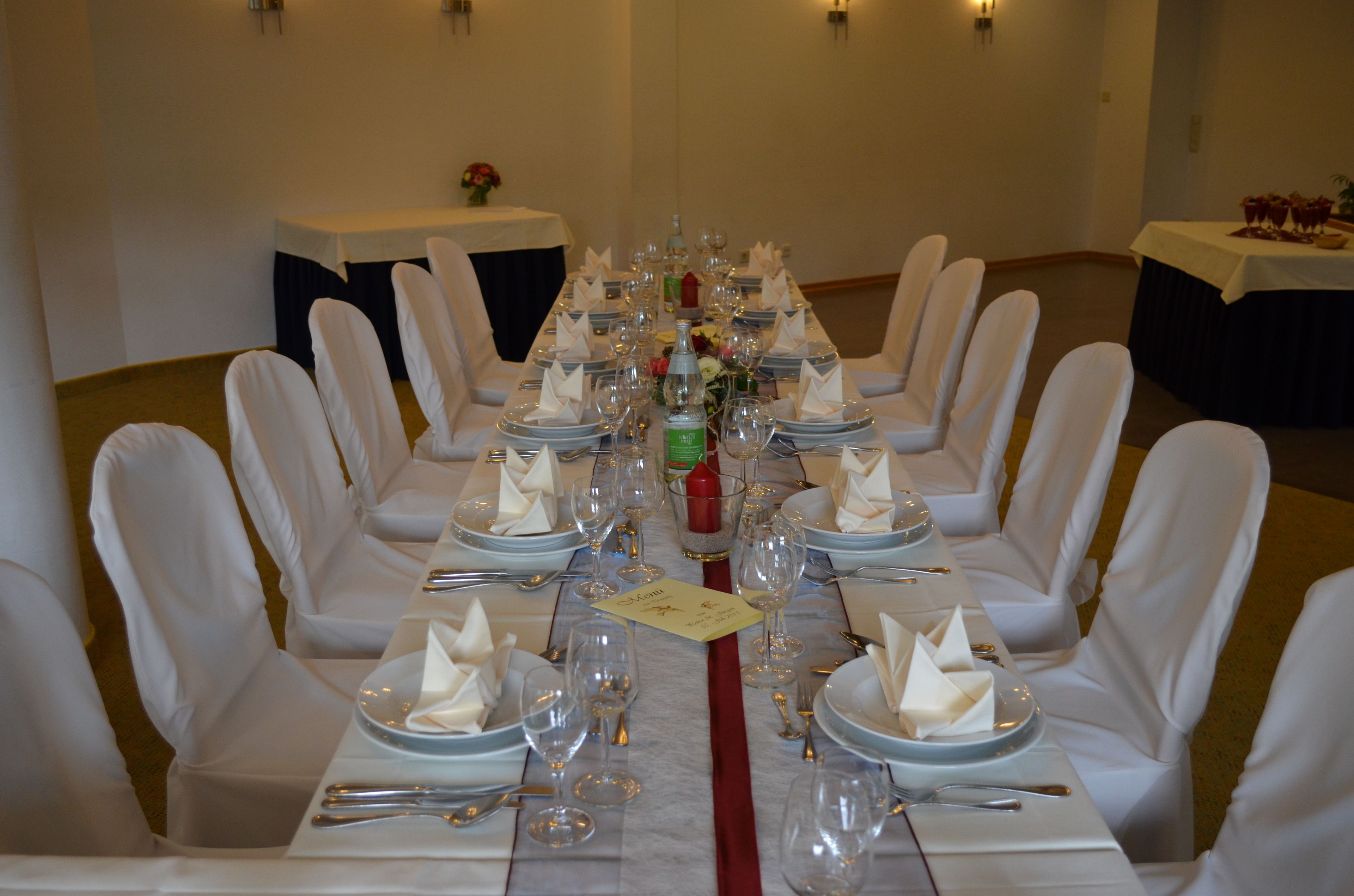 A banquet table set for a formal event with white chairs, plates, and glassware.