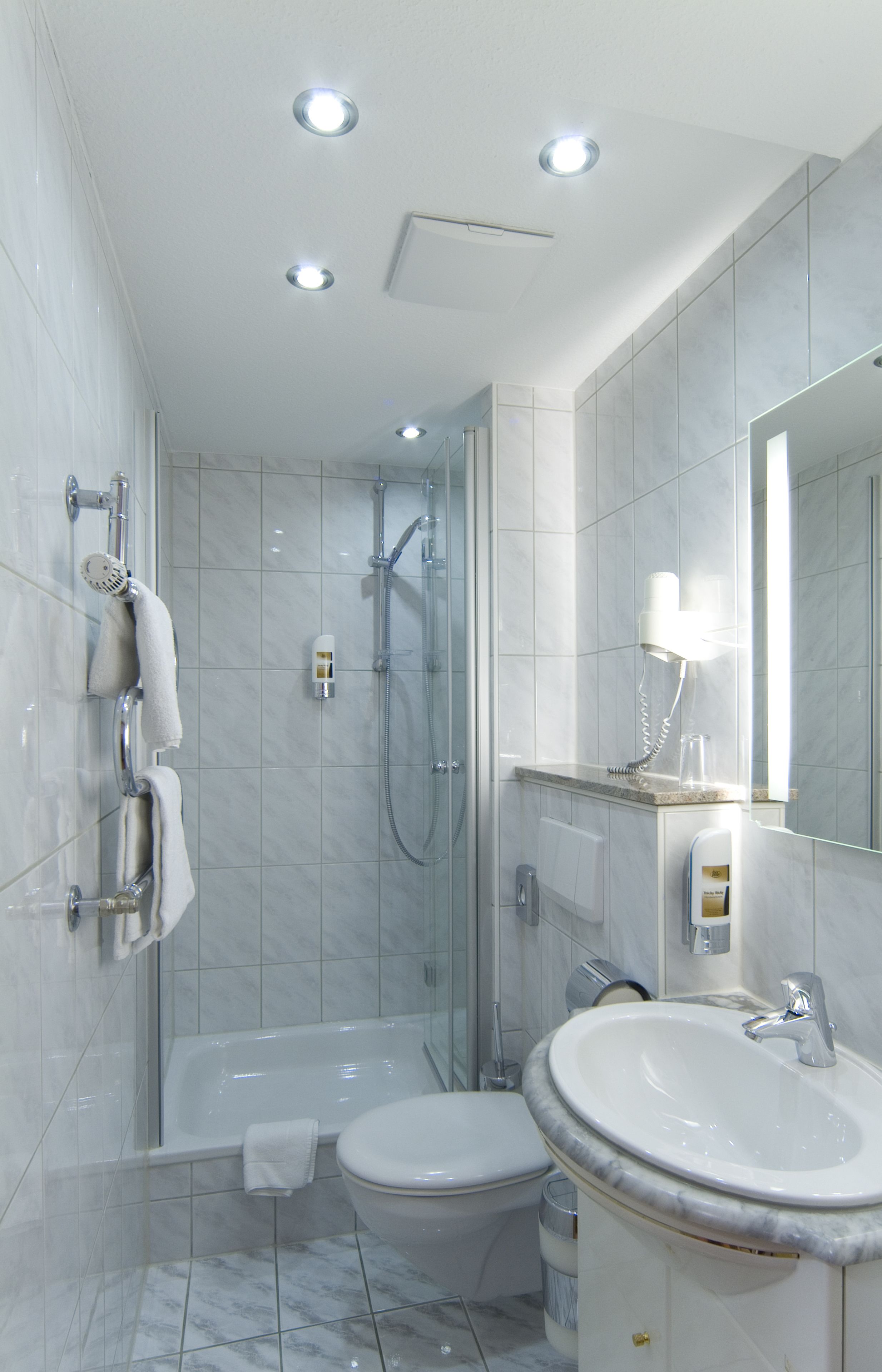 A modern bathroom with a bathtub, toilet, and sink, featuring a glass shower enclosure and a large mirror.