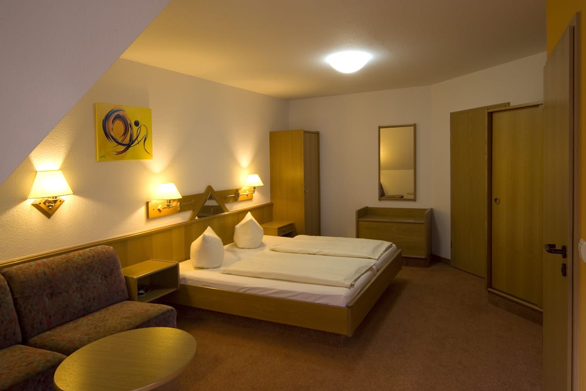 A hotel room with a bed, a sofa, a small table, a dresser, and a mirror.