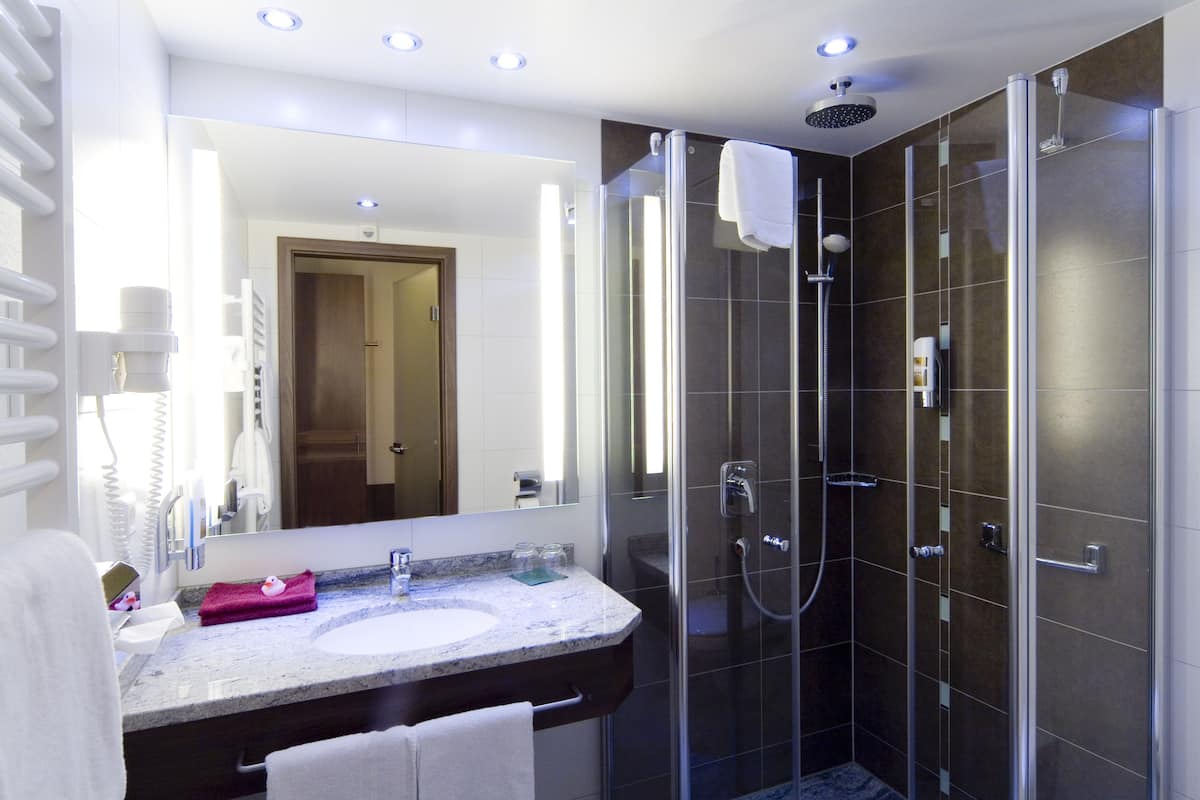 A modern bathroom with a glass-enclosed shower, a marble sink, and a large mirror.