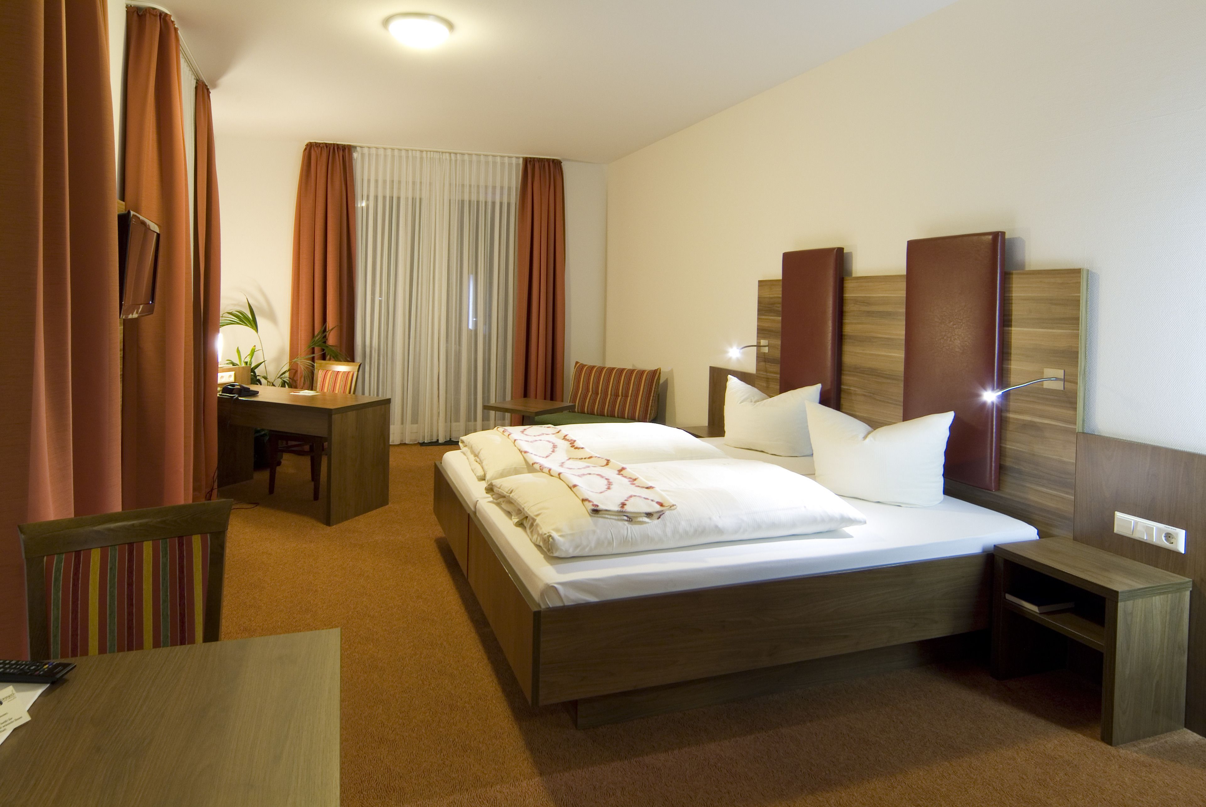 A hotel room with a bed, bedside tables, a desk, and a chair.