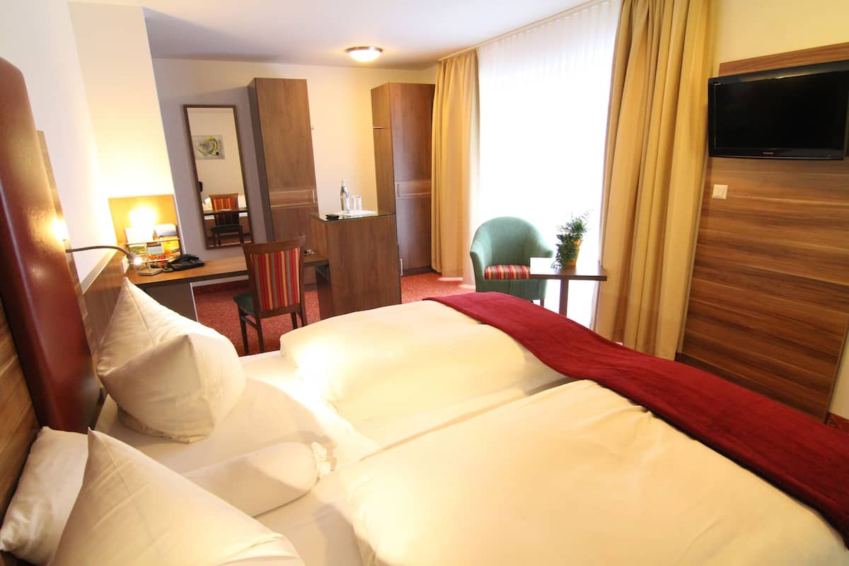 A hotel room with a large bed, a desk with a chair, a television, and a small table with a plant.