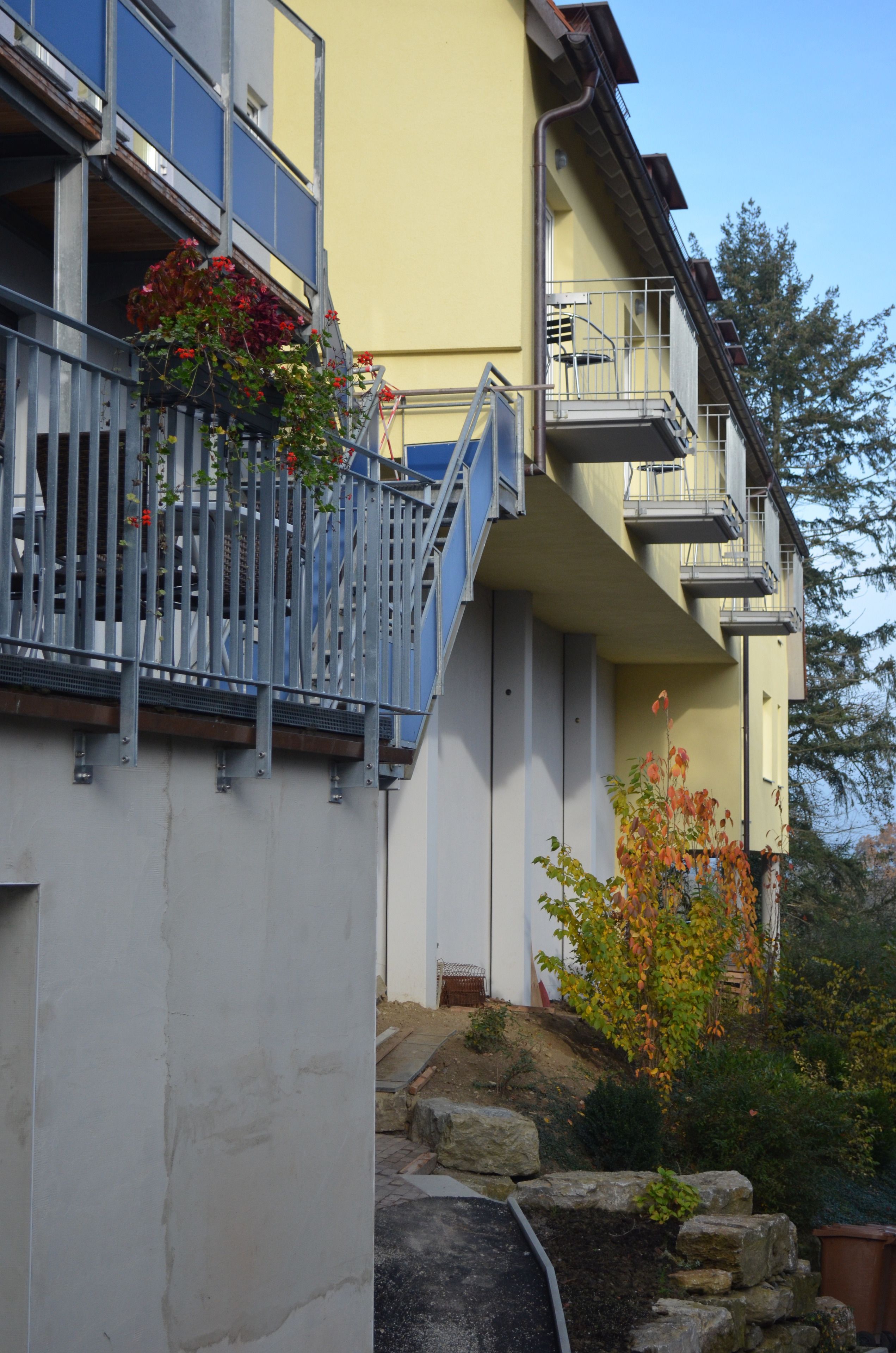Un edificio de varios pisos con balcones, una escalera y un jardín con rocas y plantas.