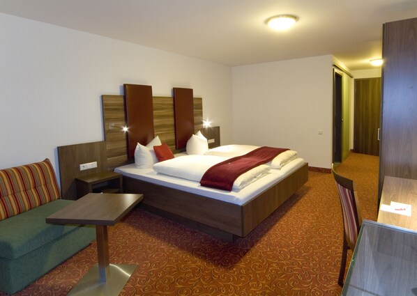 A hotel room with a large bed, a small table, a sofa, and a mirror.