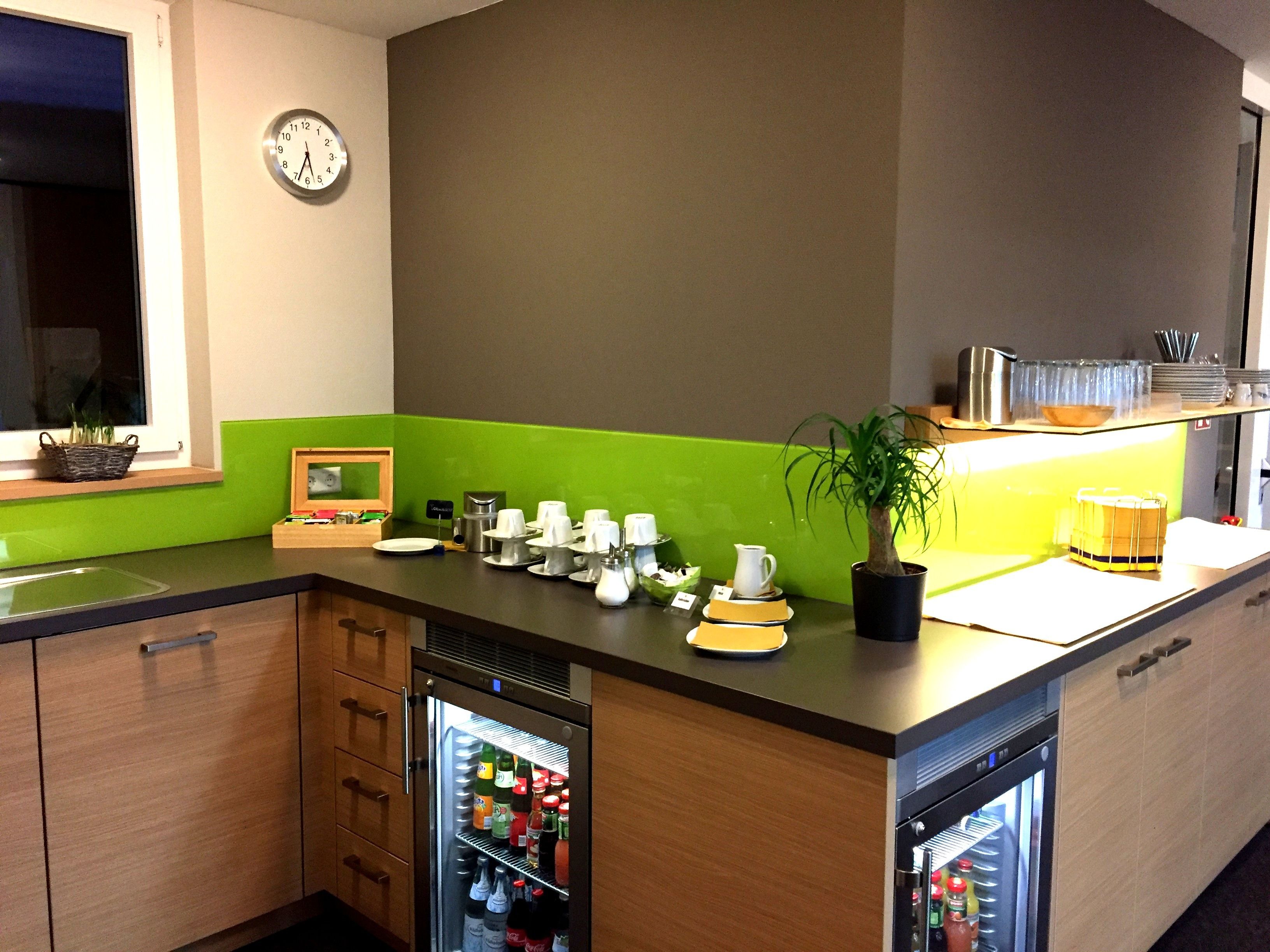 A kitchen with a clock, a refrigerator, a sink, and a green backsplash.