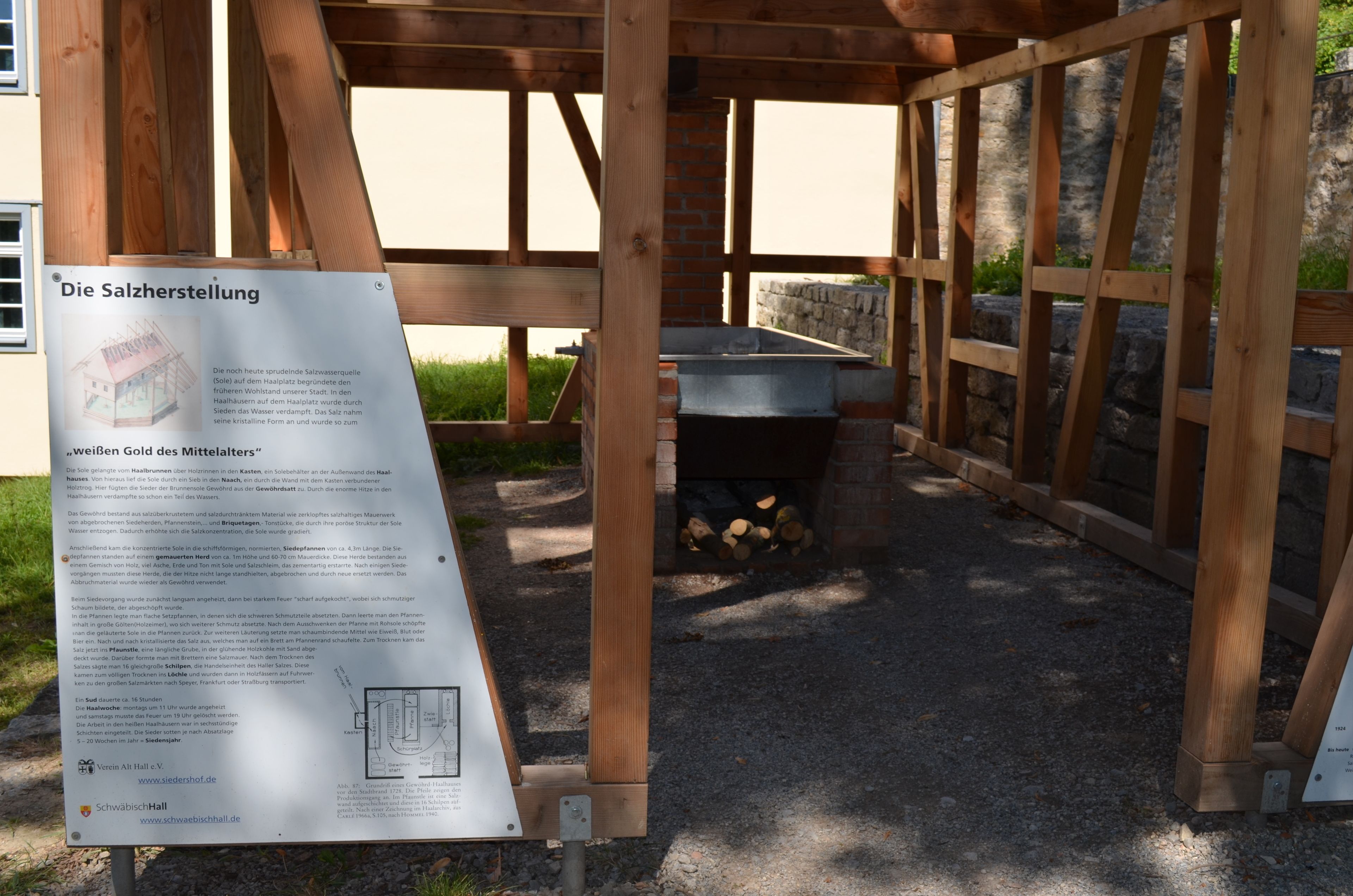 Una estructura de pérgola de madera con chimenea de ladrillo y un cartel que detalla la historia de un aljibe salinero.