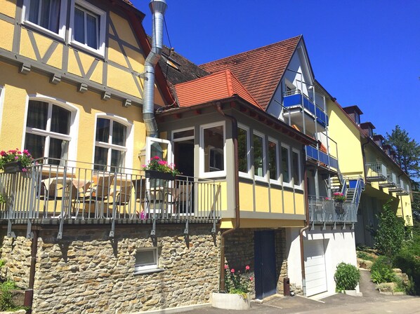 A traditional European building with a stone facade, multiple windows, and a balcony with outdoor seating.