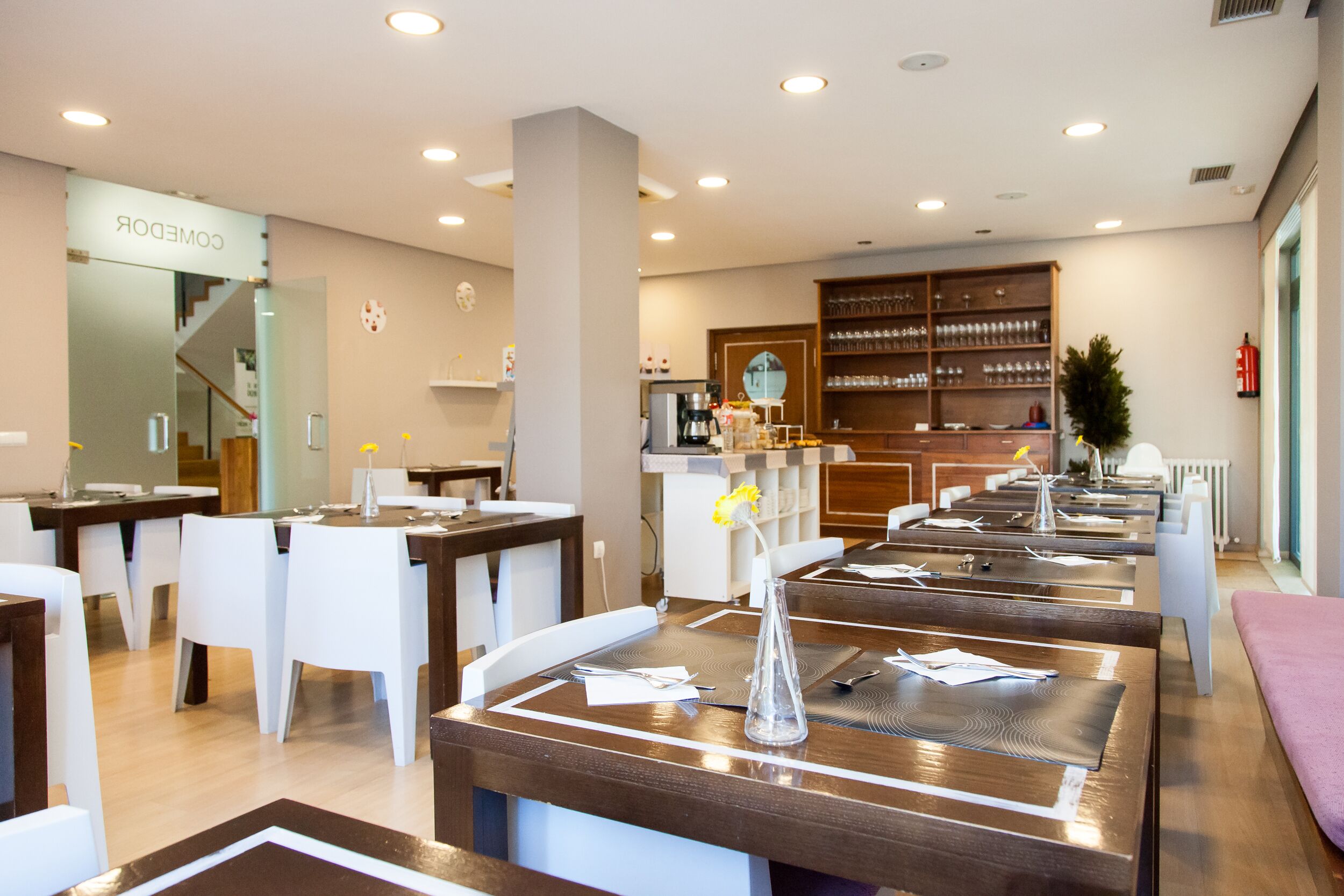 Un restaurant doté de nombreuses tables, de chaises blanches et d’un bar avec des étagères remplies de verres.