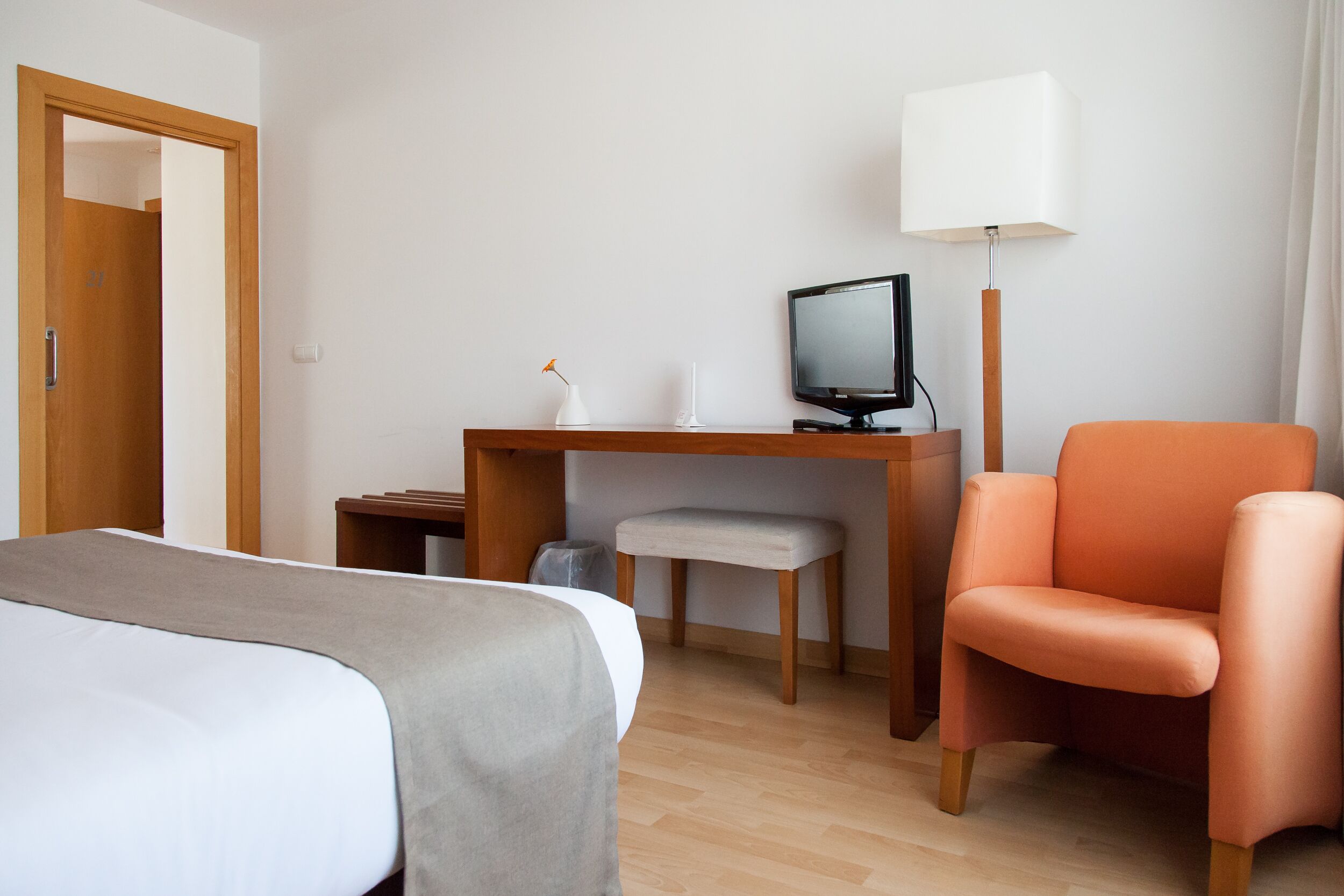 A hotel room with a bed, a desk with a computer, a chair, and a lamp.