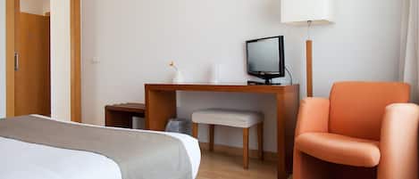 A hotel room with a bed, a desk with a computer, a chair, and a lamp.