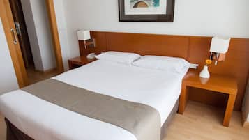 Une chambre d’hôtel avec un grand lit, une tête de lit en bois, du linge de lit blanc, une table de chevet avec une lampe et une œuvre d’art encadrée au mur.