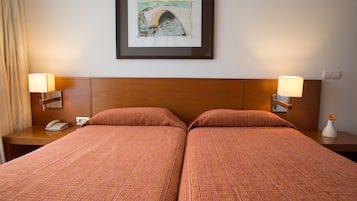 Een hotelkamer met twee bedden, een ingelijst schilderij aan de muur, nachtlampjes, een telefoon en een vaas met bloemen.
