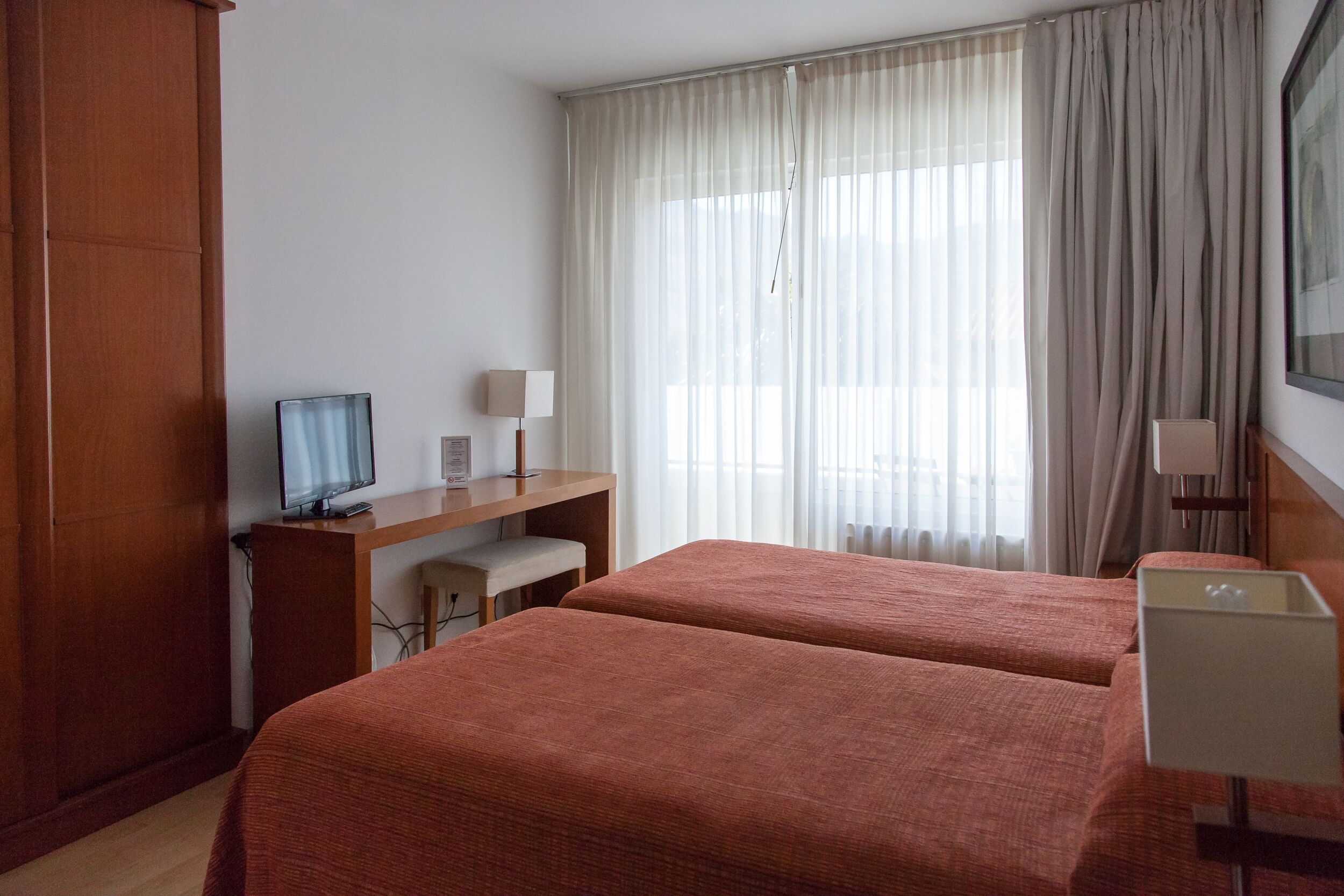 Habitación de hotel con dos camas, un escritorio con computadora, televisión y ventana con cortinas.
