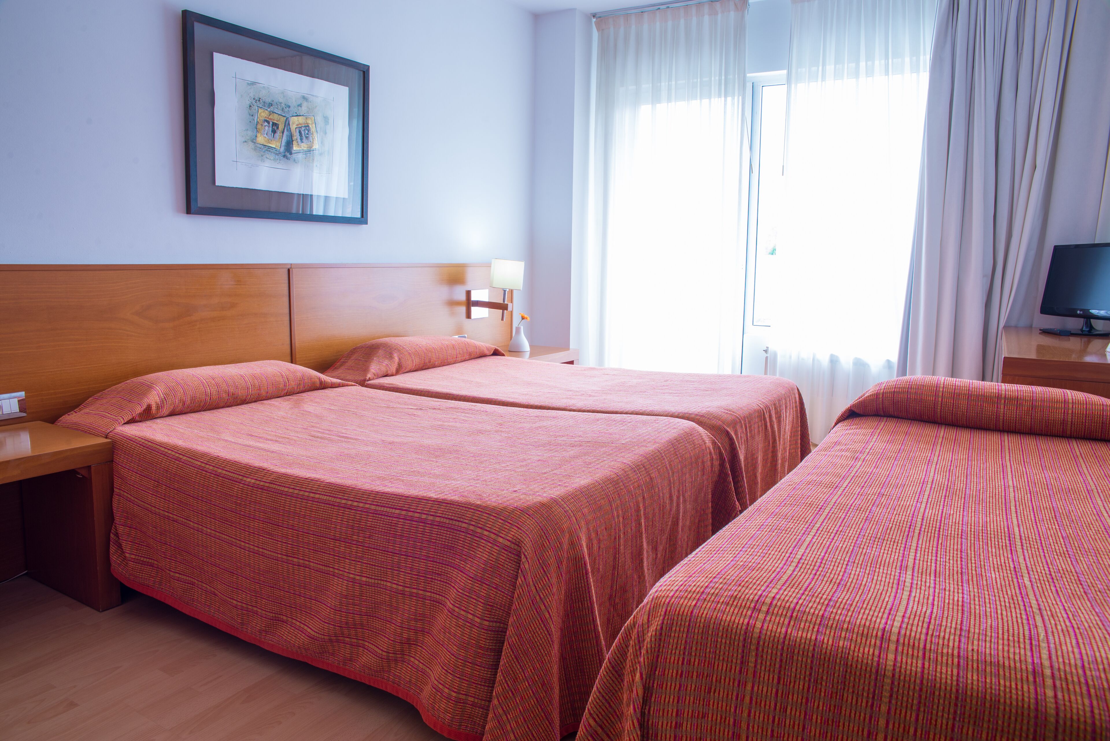 Een hotelkamer met twee bedden, een houten hoofdbord, een nachtkastje met een lamp en een lijst aan de muur.