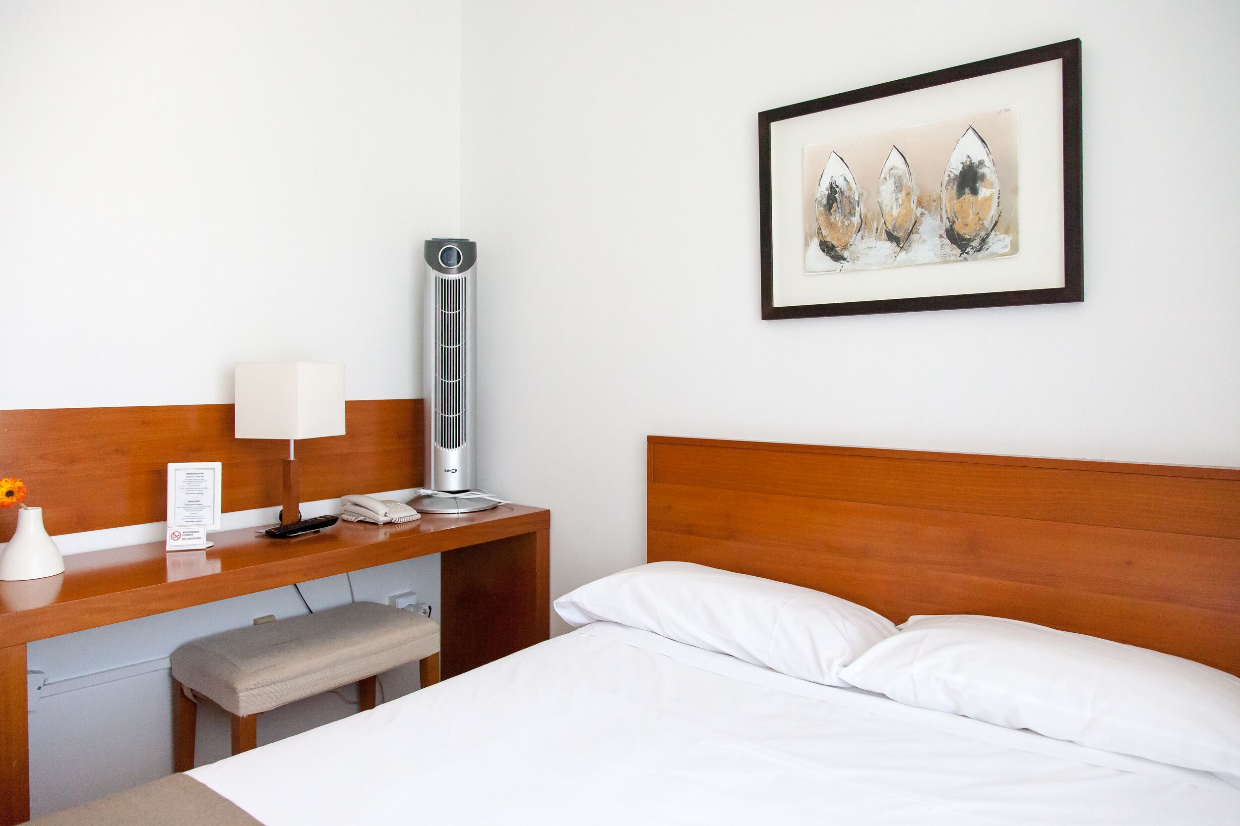 Une chambre d’hôtel avec une tête de lit en bois, une table de chevet avec une lampe, un téléphone et une œuvre d’art encadrée accrochée au mur.