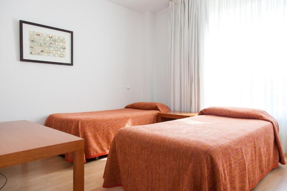 A room with two beds, a small table, and a framed picture on the wall.