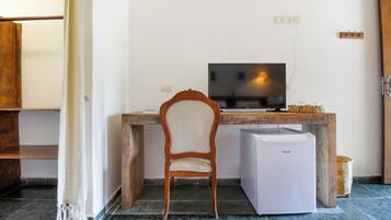 Une pièce comprenant un bureau en bois, un téléviseur, un réfrigérateur blanc et une chaise.