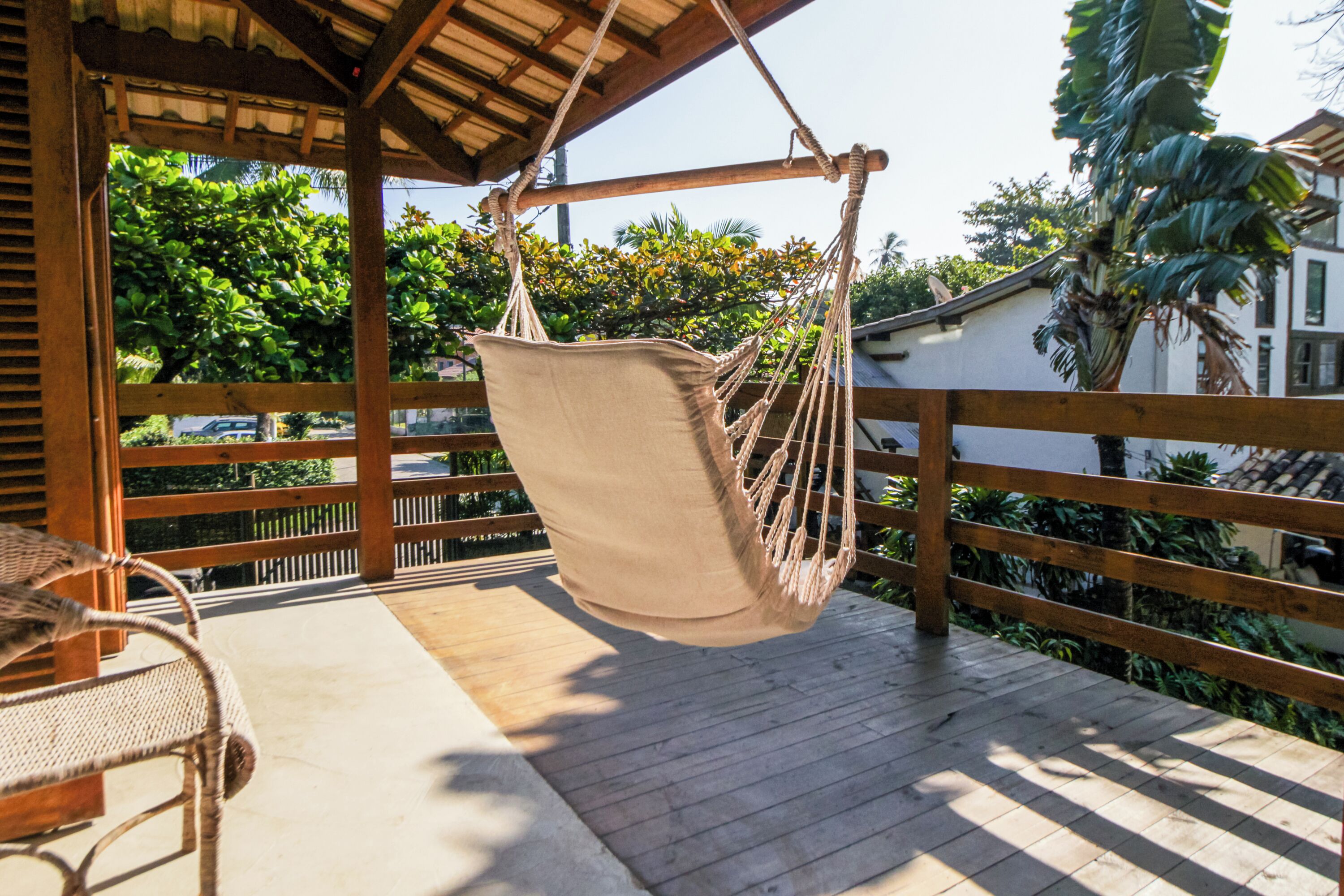 A wooden deck with a hanging hammock chair and a wicker table.