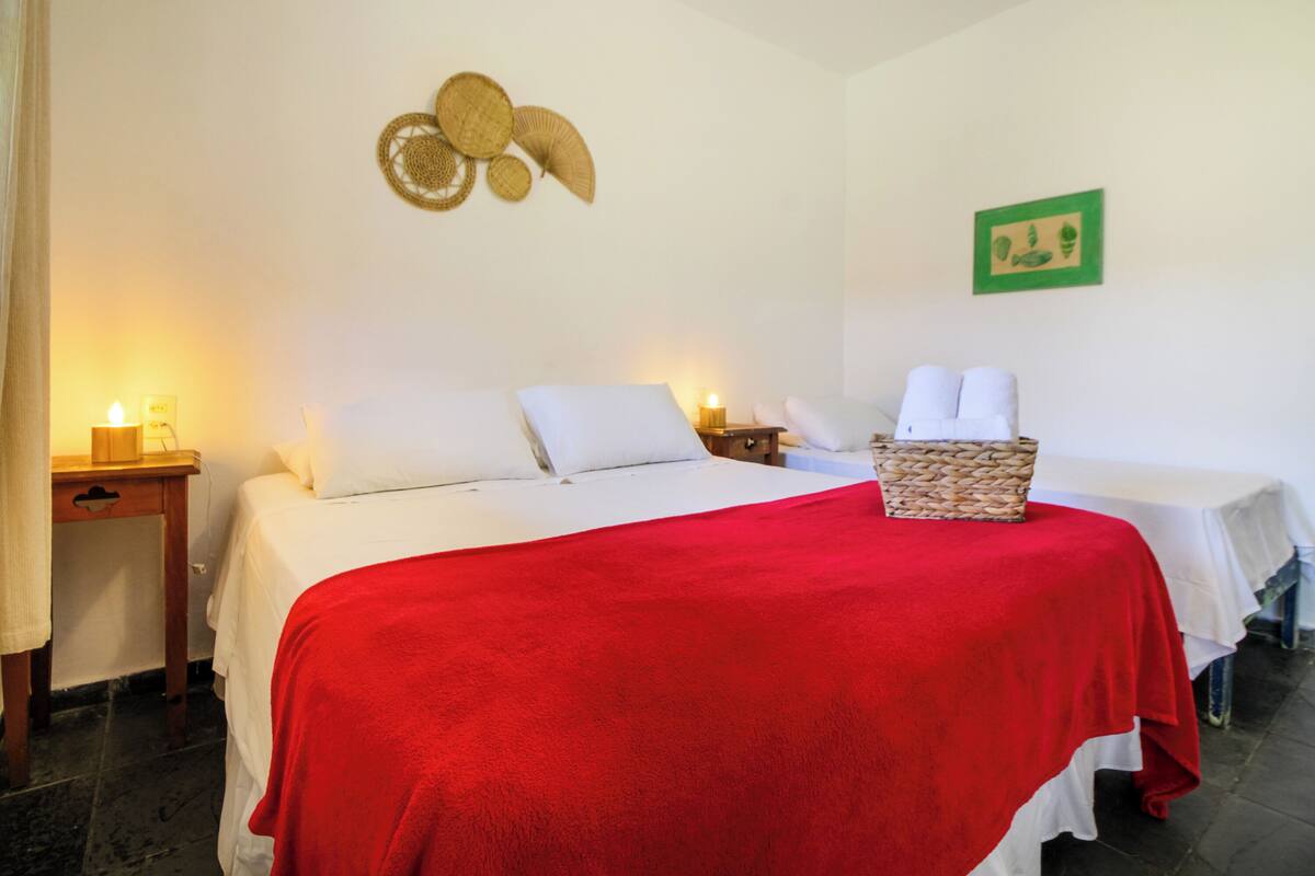 A hotel room with a bed, a red blanket, a basket of towels, and wall decorations.