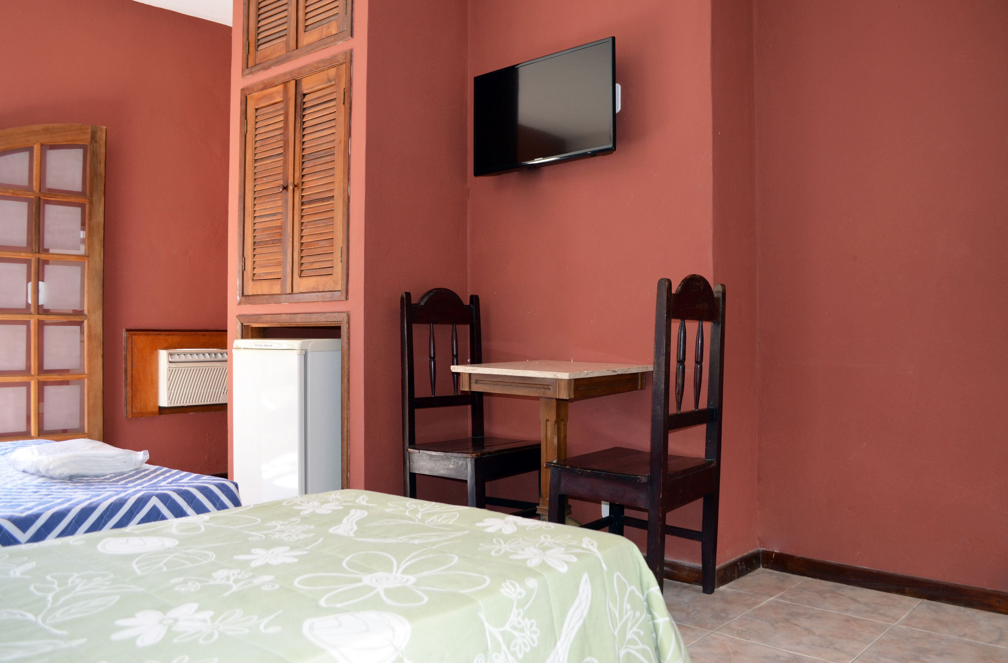 A room with a bed, a desk, two chairs, a television, and a window with shutters.