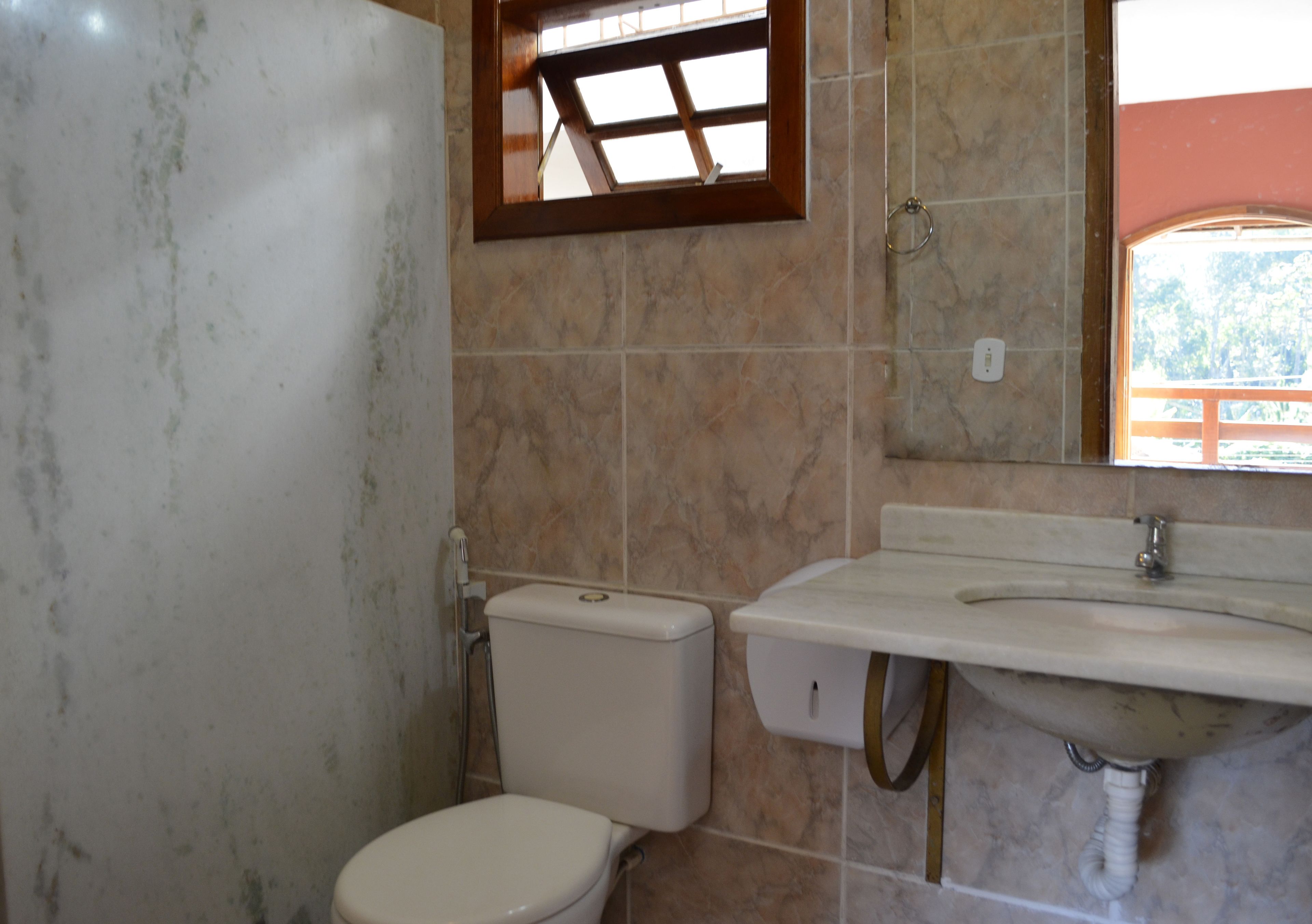 Un baño con inodoro, lavamanos y una ventana sobre el lavamanos.