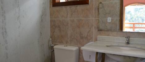 Un baño con inodoro, lavamanos y una ventana sobre el lavamanos.