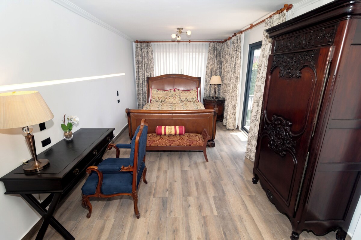 A bedroom with a bed, a desk with a lamp, a chair, and a wardrobe.