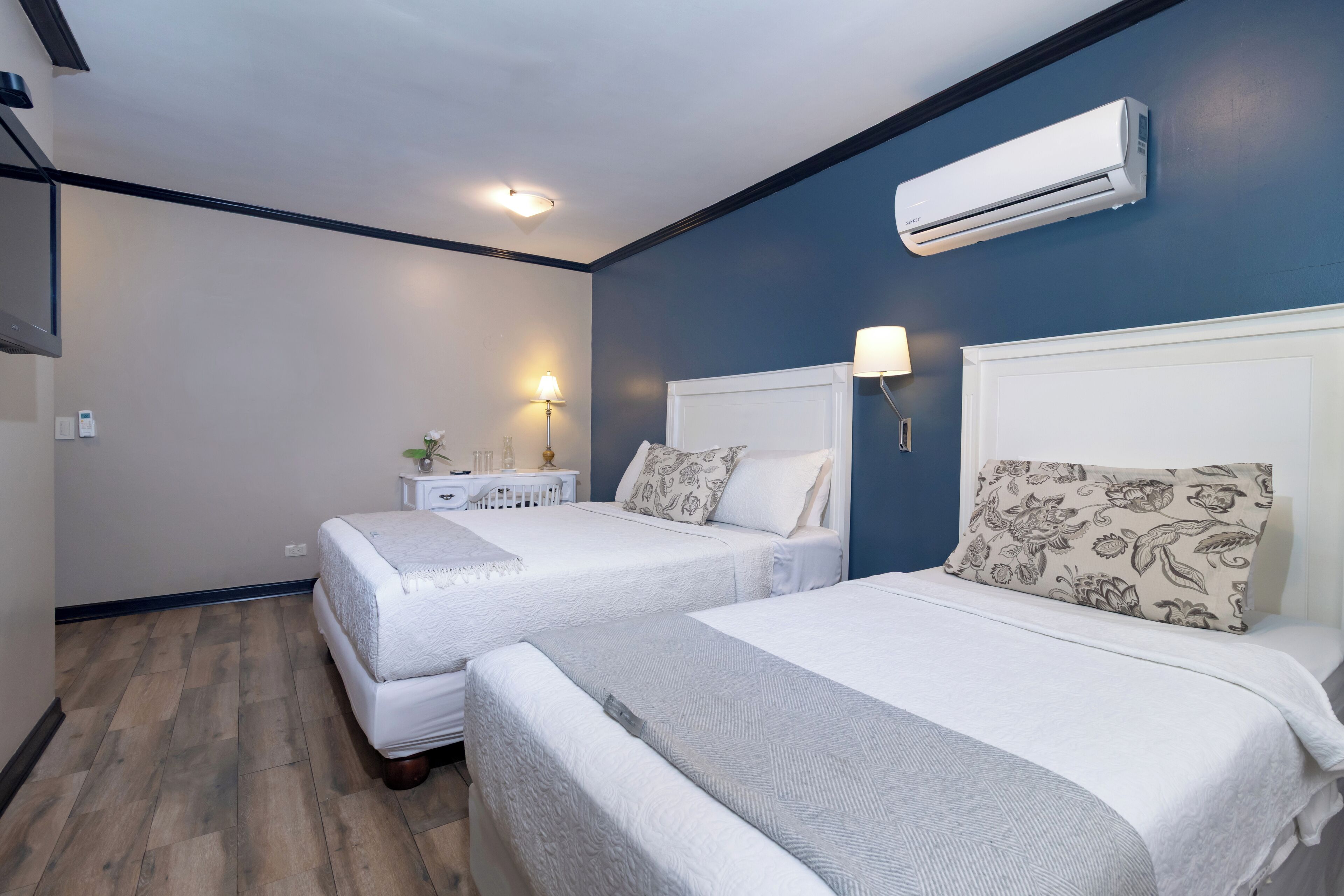 A hotel room with two beds, a white nightstand, a lamp, and an air conditioning unit.