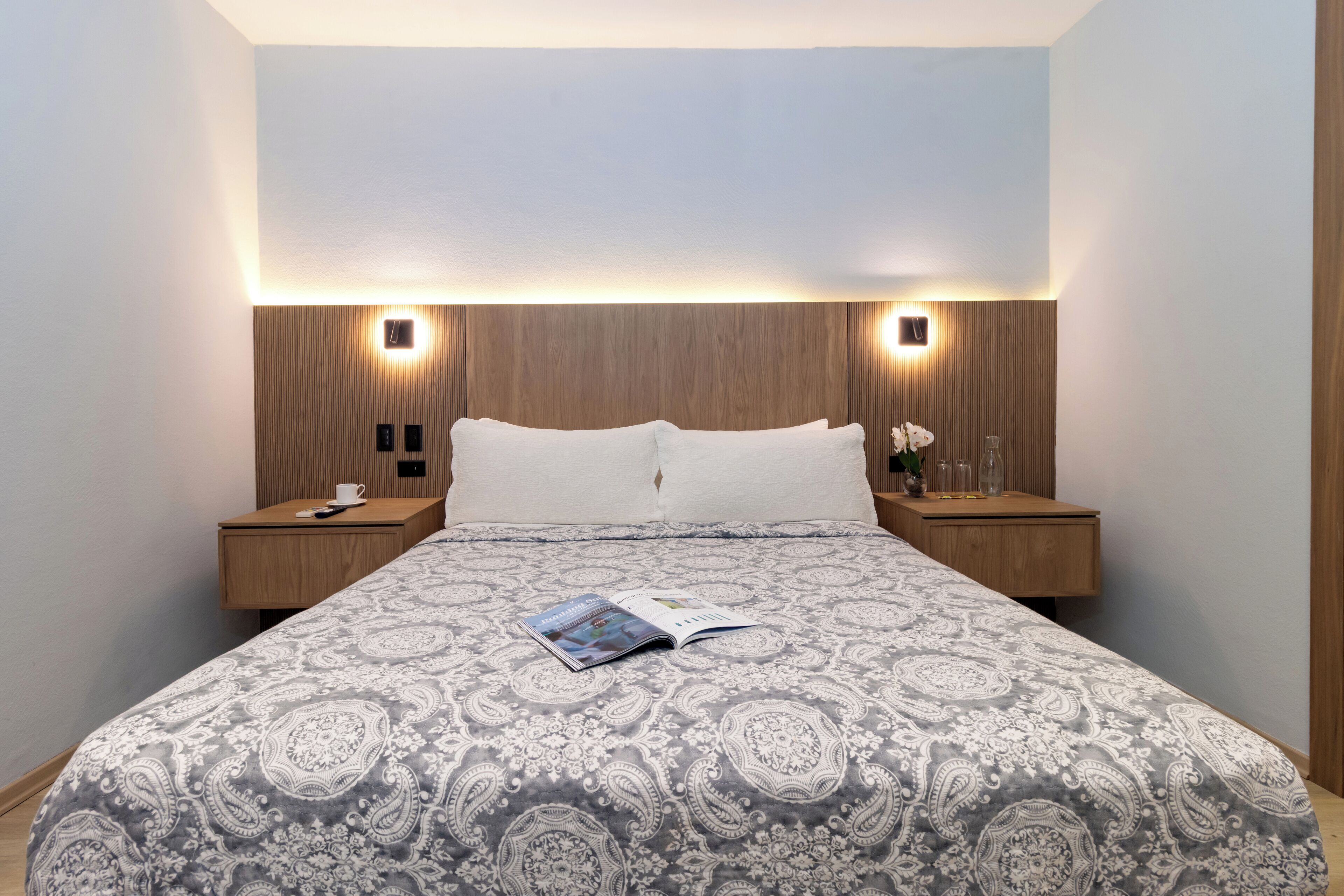 Un lit bien fait, recouvert d’une couvre-lit à motifs, deux tables de chevet avec des lampes et un luminaire fixé au mur.