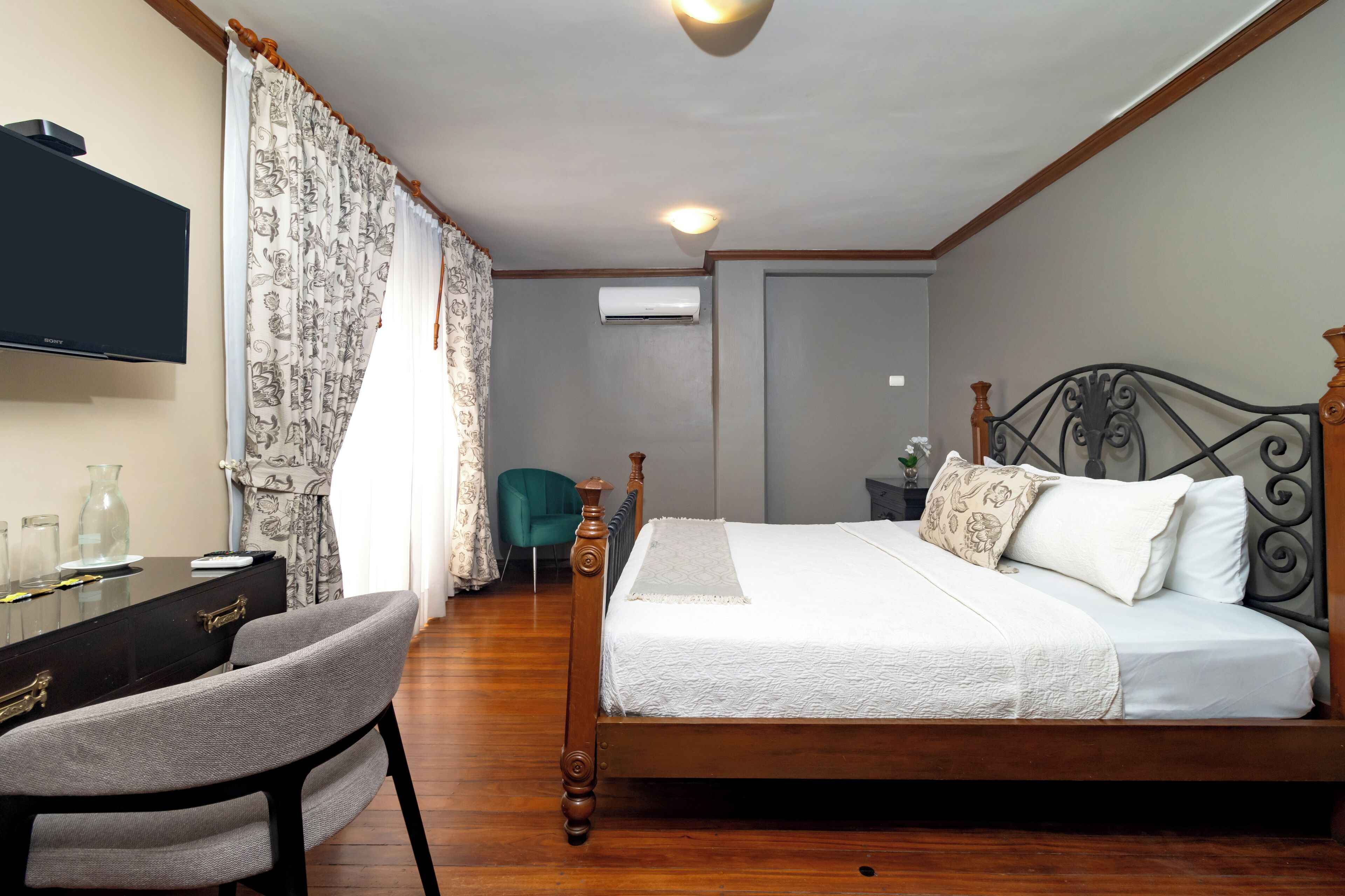 Une chambre à coucher avec un lit en bois, un bureau avec une chaise, une télévision et un fauteuil de couleur turquoise.